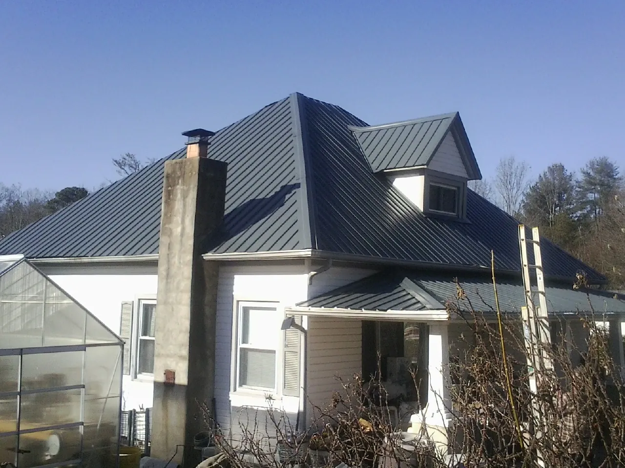 Dark blue standing seam metal roof on a white farmhouse with dormer — Slate & Tile Roof Repair by Roofing Brothers in Grand Junction
