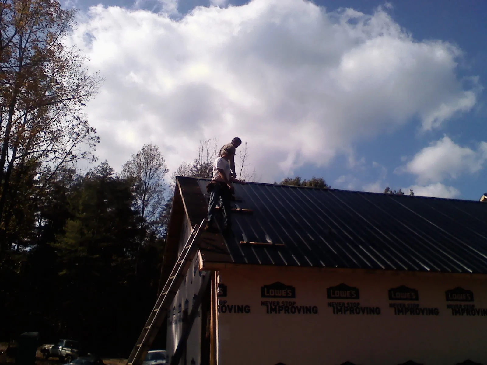 Roofer fastening dark metal panels high against a cloudy sky, from a Roof Inspection job in Grand Junction